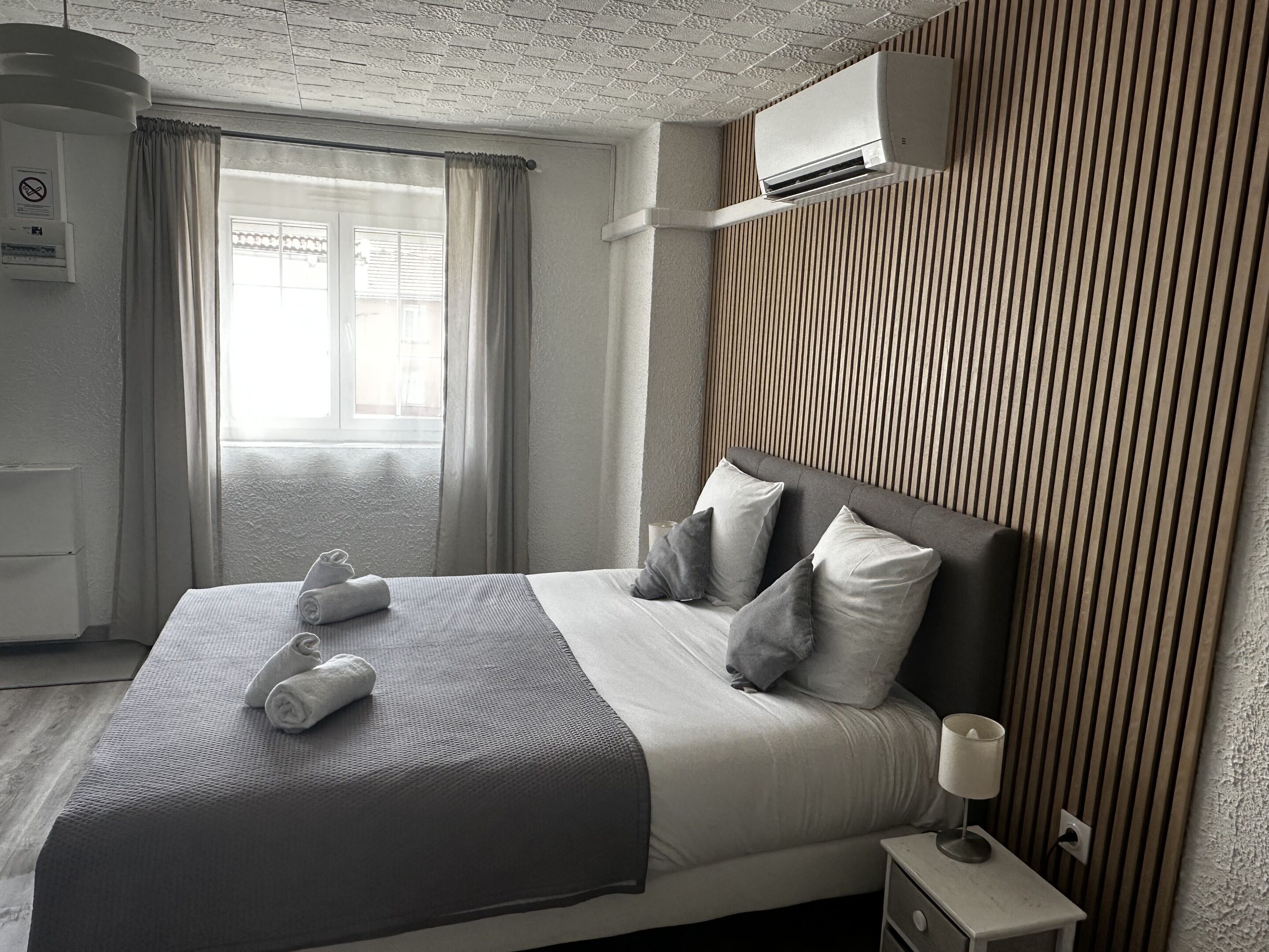 A neatly made bed with pillows and towels, a bedside table with a lamp, and a window with curtains.