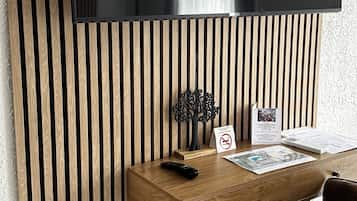 Una habitación moderna con un muro de listones de madera, un televisor montado, un escritorio con un control remoto, una silla y una pequeña mesa con un cartel.