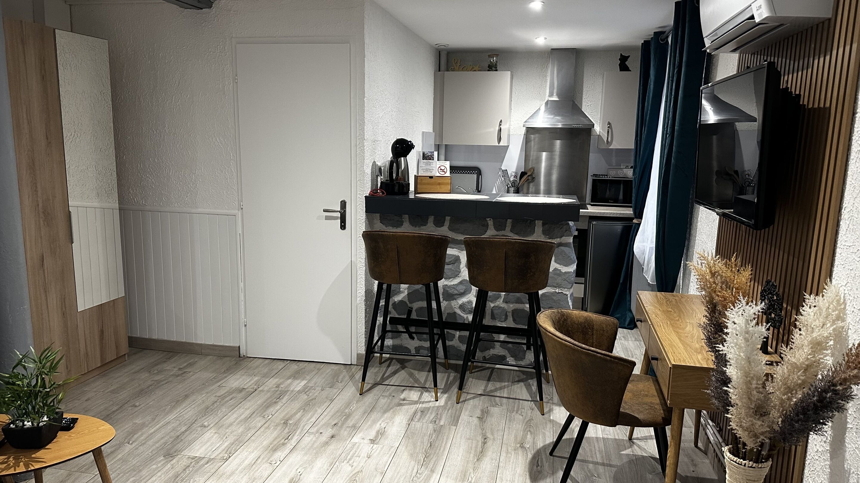 Una cocina compacta con una isla central, un comedor con dos sillas y una mesita con una planta.