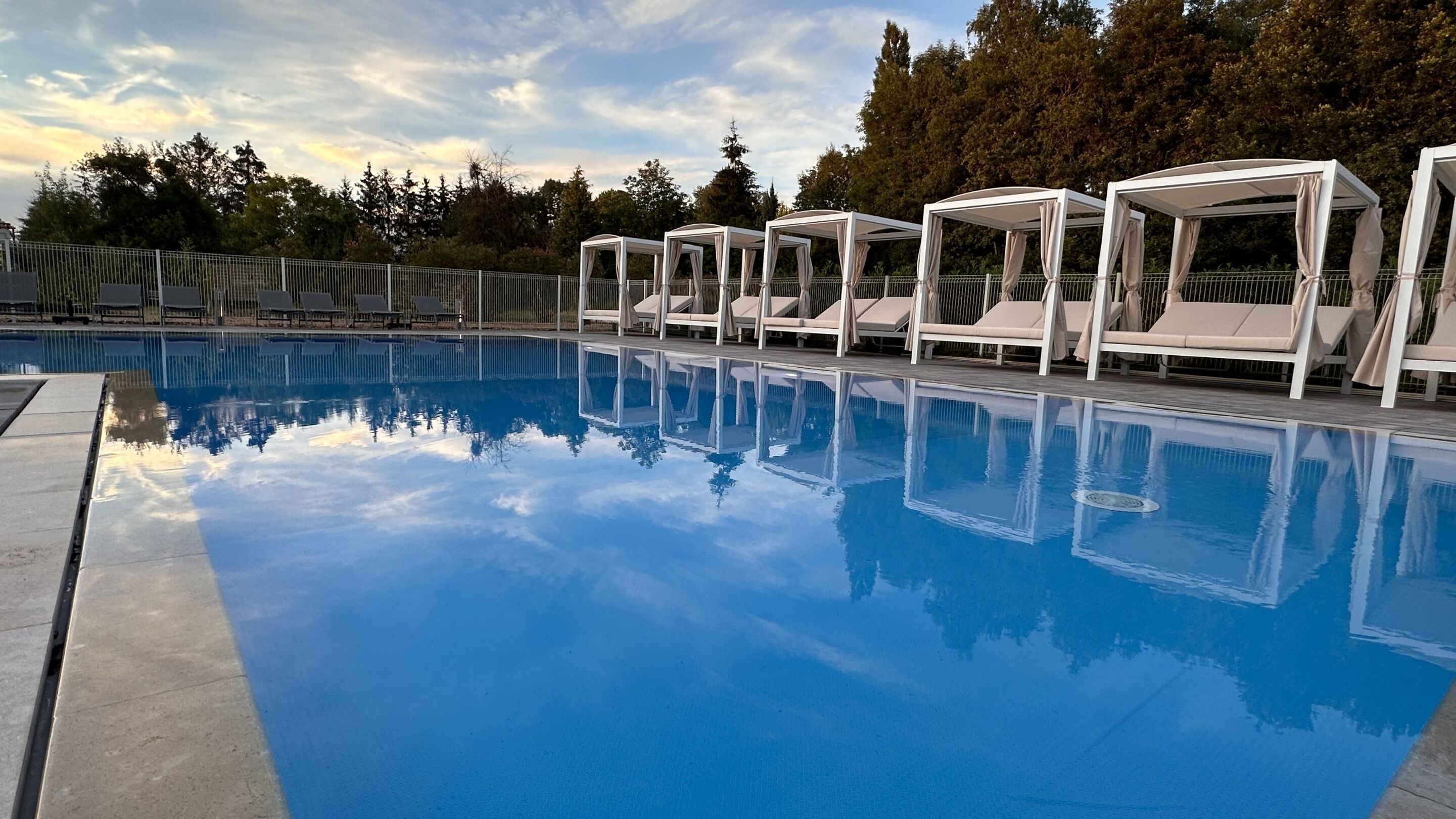 A swimming pool with clear blue water, surrounded by white lounge chairs and covered seating areas.