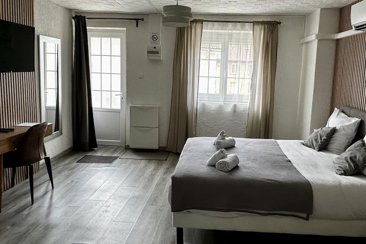 A bedroom with a bed, a desk, a chair, a TV, and a window with curtains.