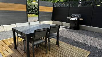 Eine Terrasse im Freien mit einem Holztisch und Stühlen, einem Grill und einem dekorativen Zaun.