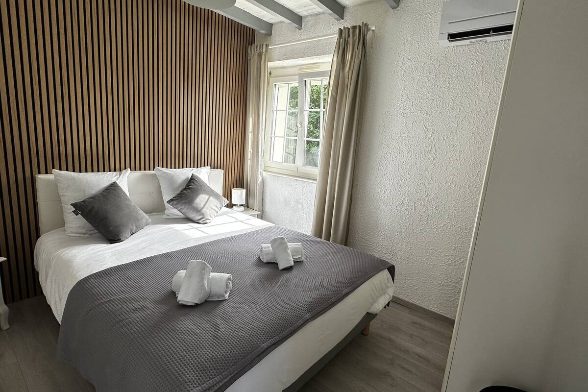 A neatly arranged hotel room with a bed, a bedside table with a lamp, and a window with curtains.