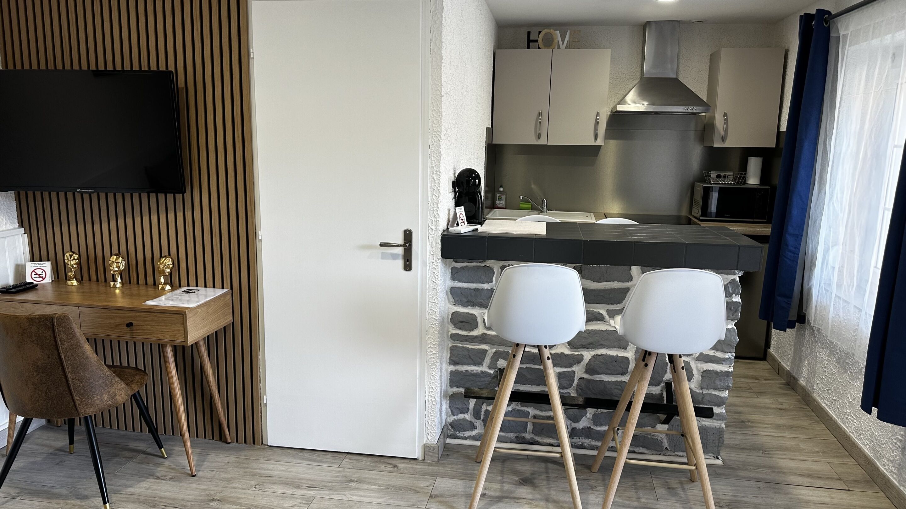 Une cuisine moderne avec un pare-feu en pierre, un téléviseur à écran plat fixé au-dessus du comptoir, et un coin repas en bois comprenant une chaise et une petite table.