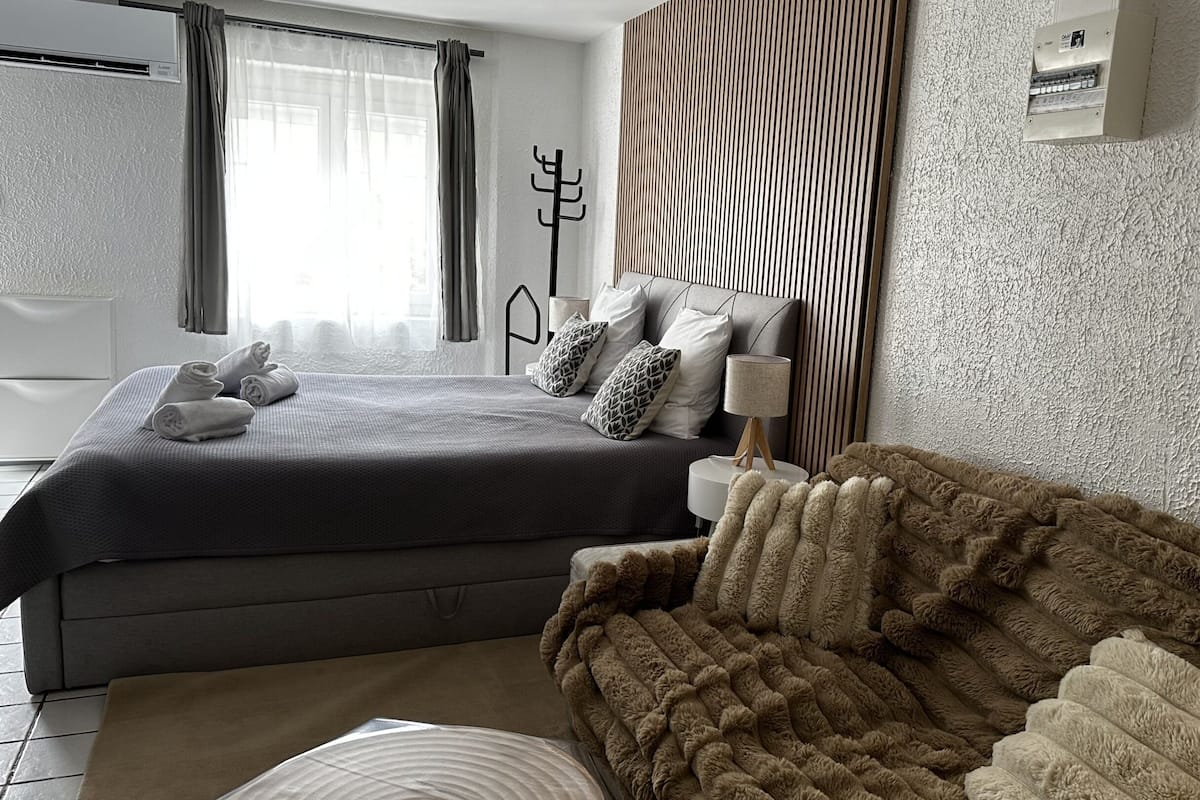 A modern bedroom with a large bed, a sofa, a lamp, and a thermostat on the wall.