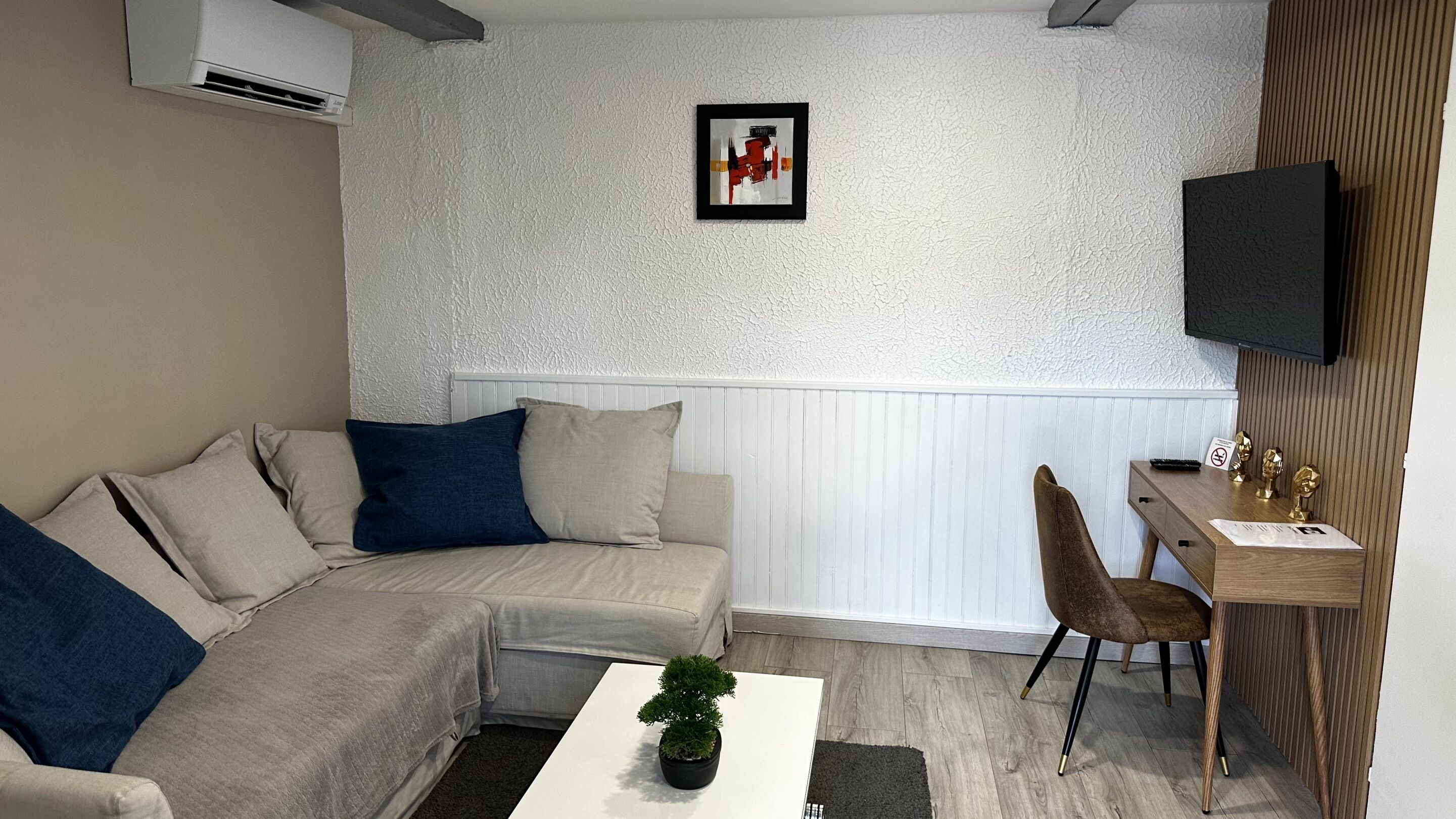 A modern living room with a sectional sofa, a small table with a plant, and a TV mounted on the wall.