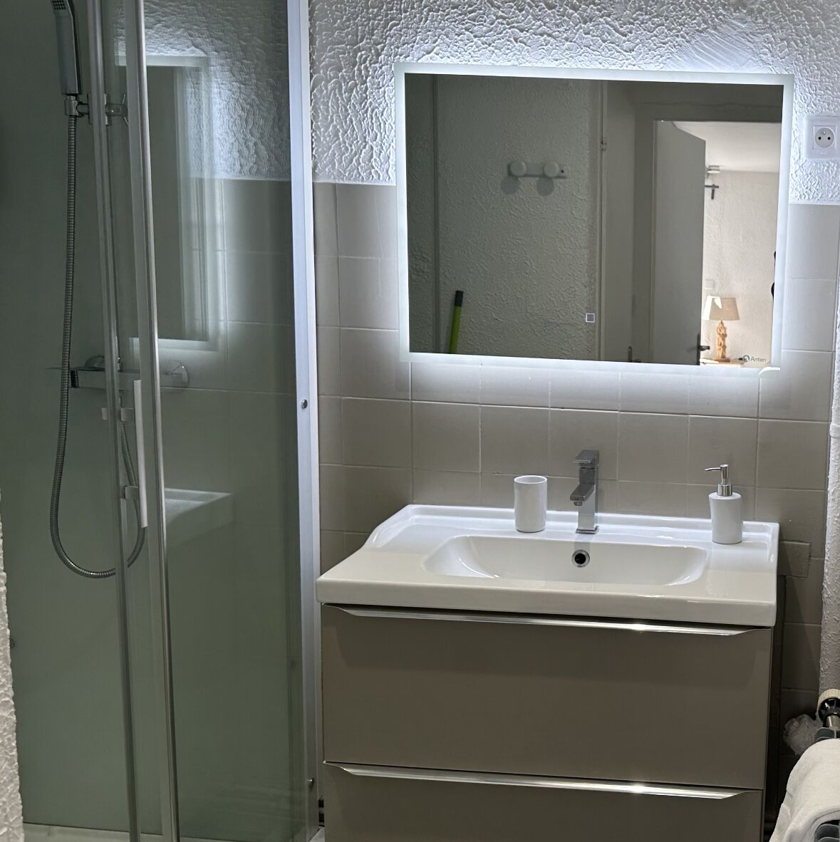 Une salle de bain avec une douche à parois de verre, un lavabo blanc avec un miroir au-dessus et un porte-serviettes.