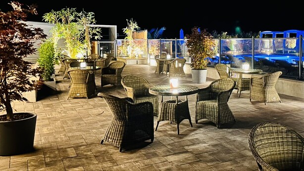 Pátio externo com mobiliário de vime, plantas em vasos e área de piscina com iluminação azul.