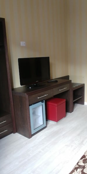 Een kamer met een donkere houten tv-standaard, een kleine koelkast en een rode opbergkist.
