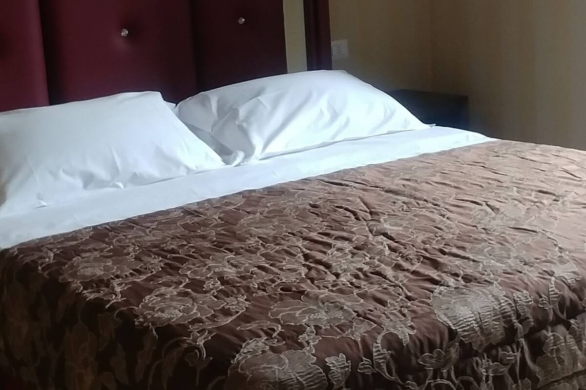 Una cama con cabecera roja, almohadas blancas y una colcha marrón con estampado floral.
