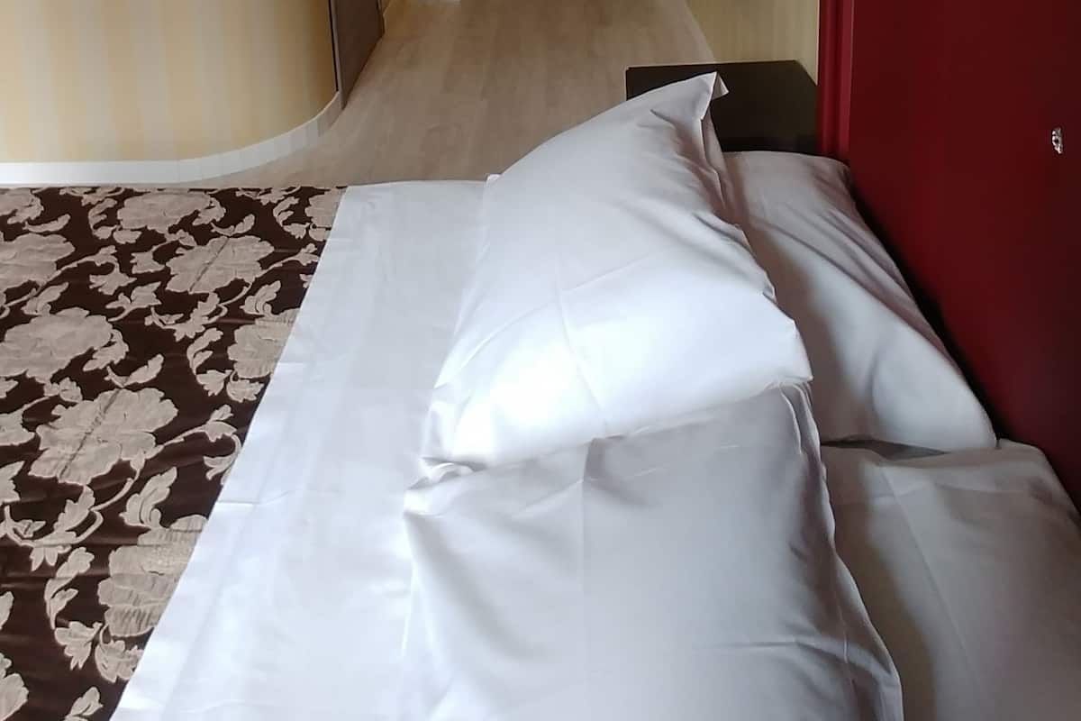 Una habitación de hotel con una cama, cabecera roja, alfombra estampada y una puerta al fondo.