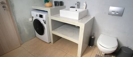 Ein kleines Badezimmer mit Waschmaschine, Waschbecken und Toilette.