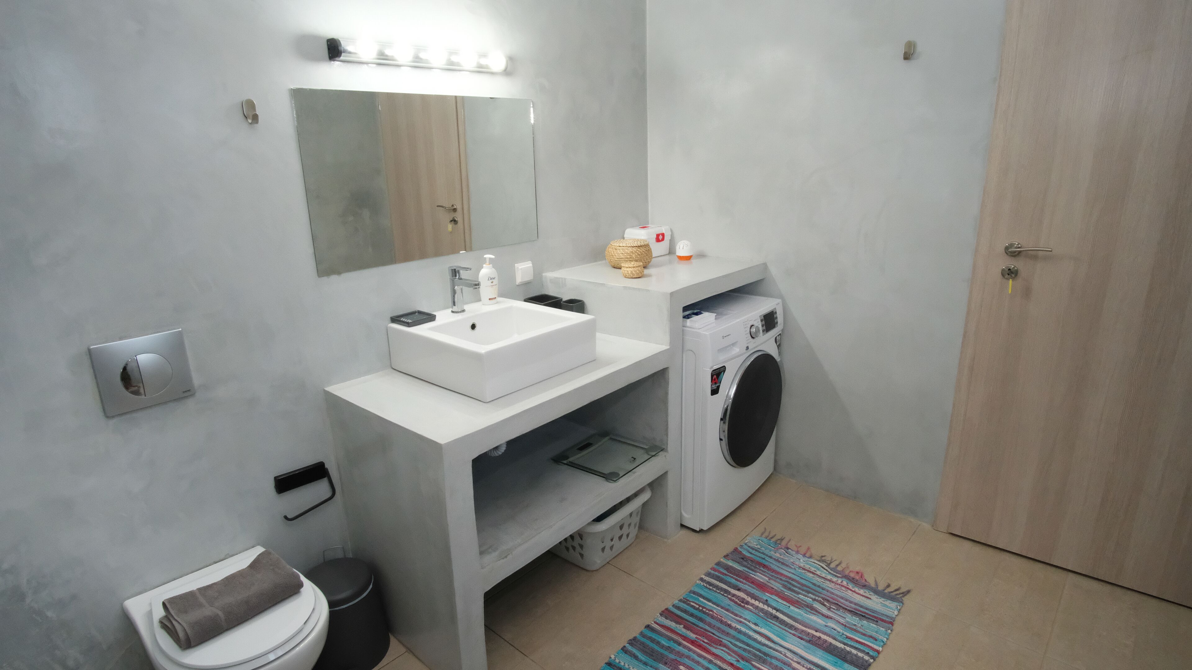 A modern bathroom with a white sink, mirror, and a washing machine.