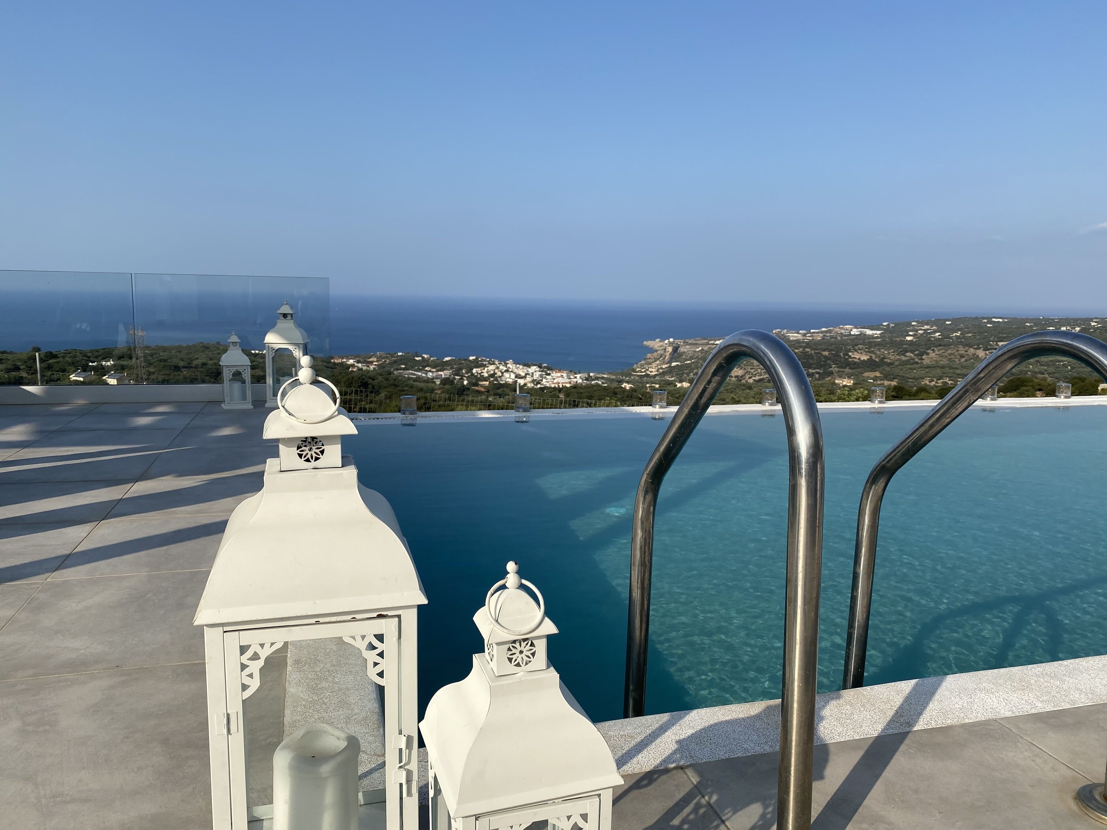 A rooftop infinity pool with a clear view of the sea and a distant coastline.