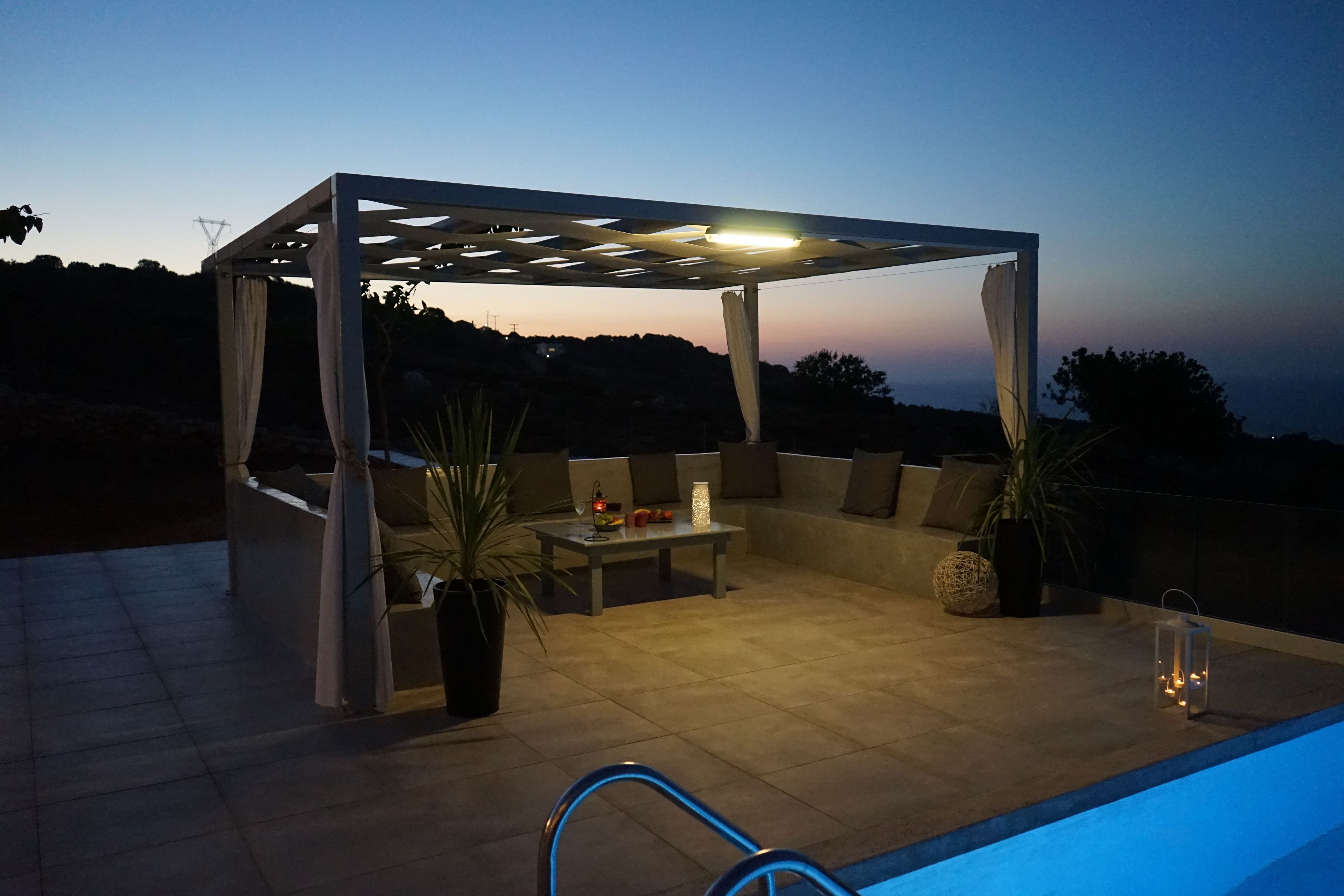 An outdoor patio with a pergola, seating, a table, and potted plants.