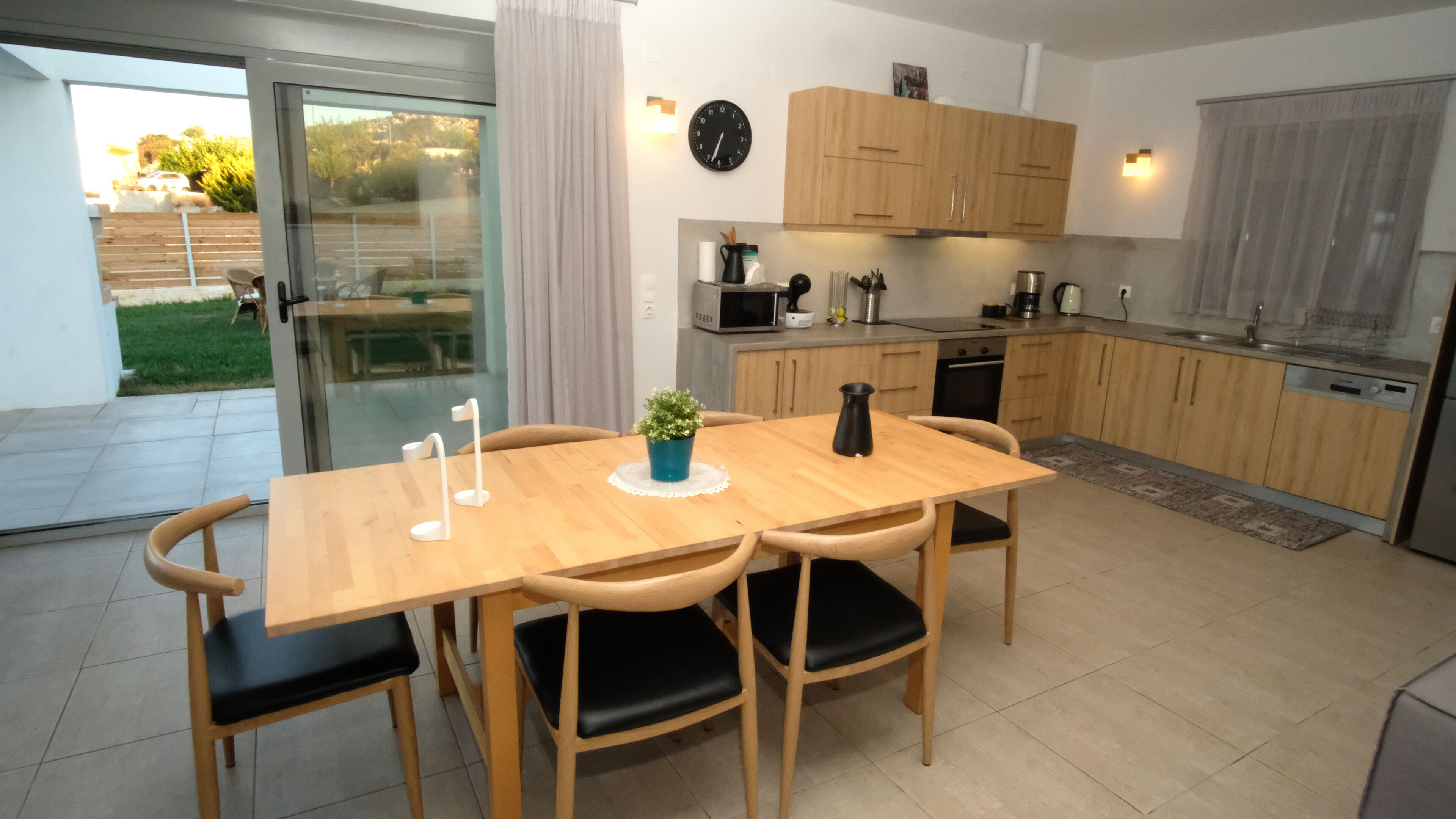 A modern kitchen with wooden cabinets, a dining table with chairs, and a view of the outdoors through a sliding glass door.