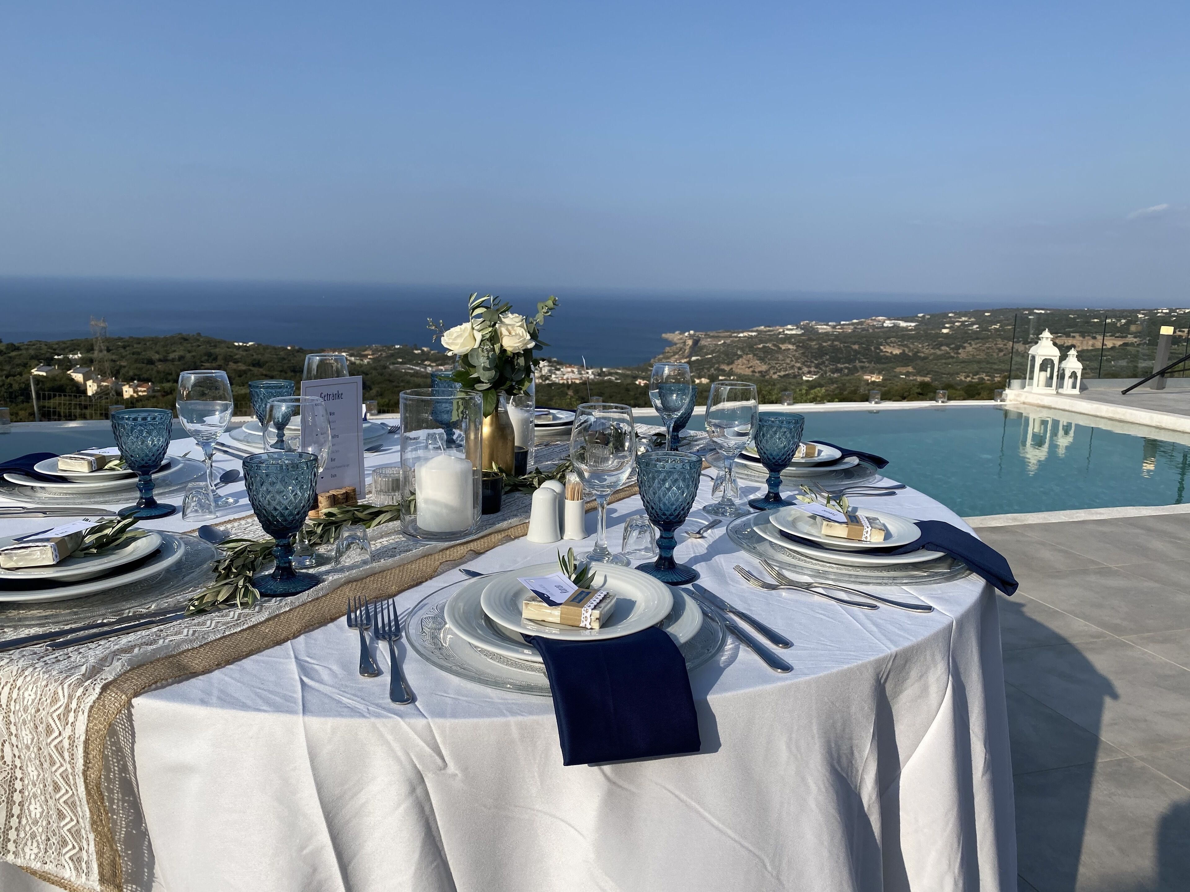 Una mesa dispuesta para una comida, con vistas al mar y colinas al fondo.