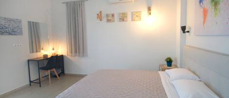 Un dormitorio con cama, escritorio y silla. Se observa una ventana con cortinas, un equipo de aire acondicionado y una lámpara en la pared.