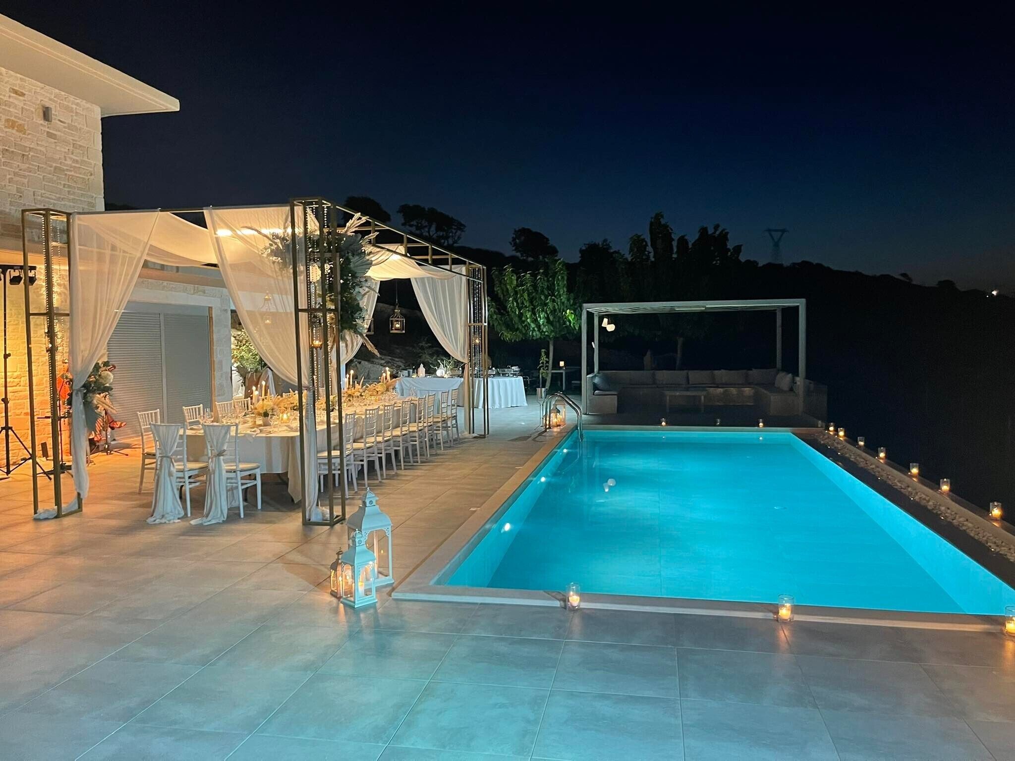 A poolside area with a covered seating area, a dining setup, and a view of the surrounding landscape.