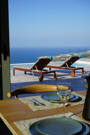 A dining table with a view of the ocean and two sun loungers. - Eva Villas (Rethymno)