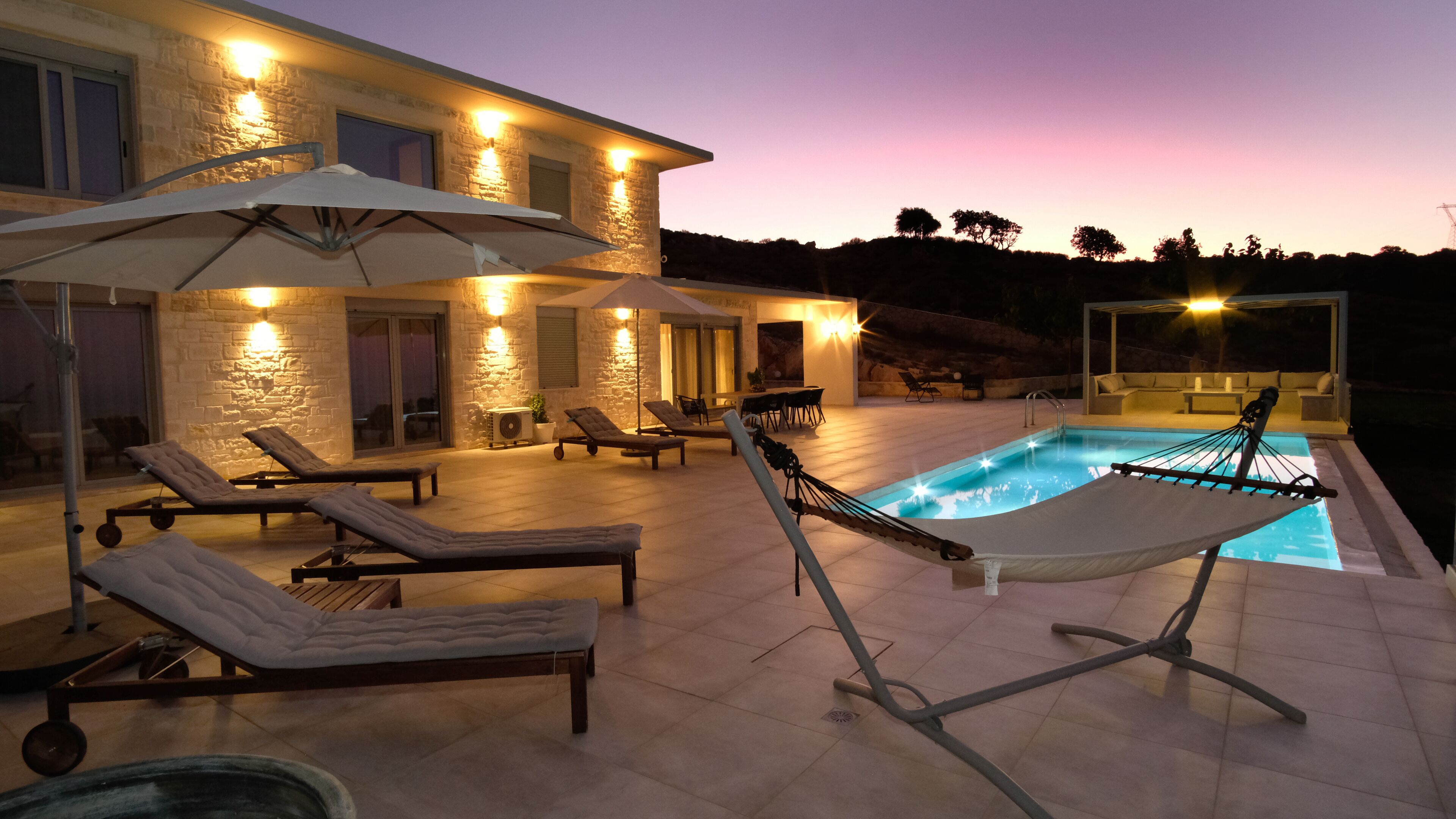 Un área junto a la piscina con sillas de descanso, sombrillas y una hamaca.