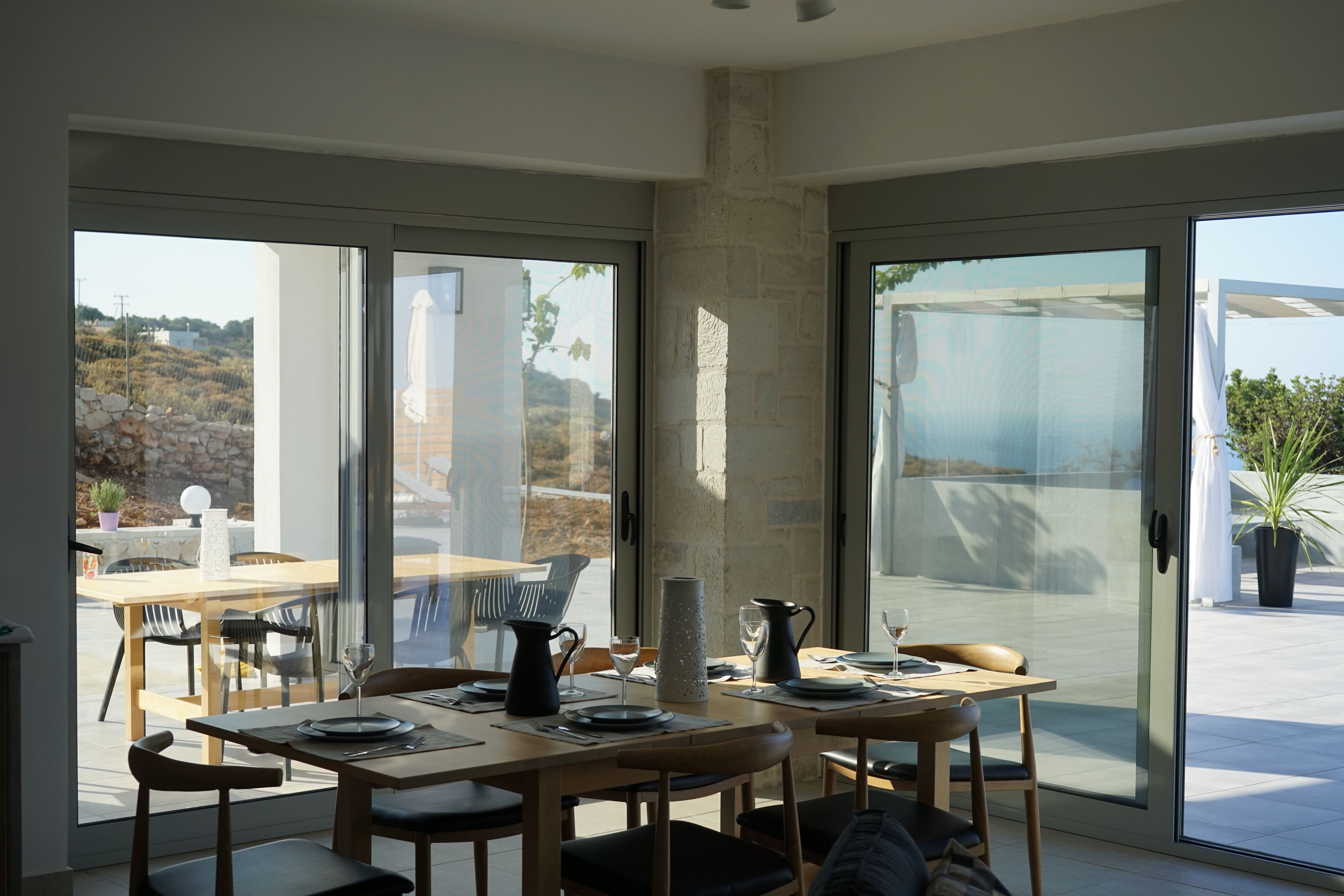 Un comedor moderno con una mesa y sillas de vidrio, un pilar de piedra y vistas al exterior.