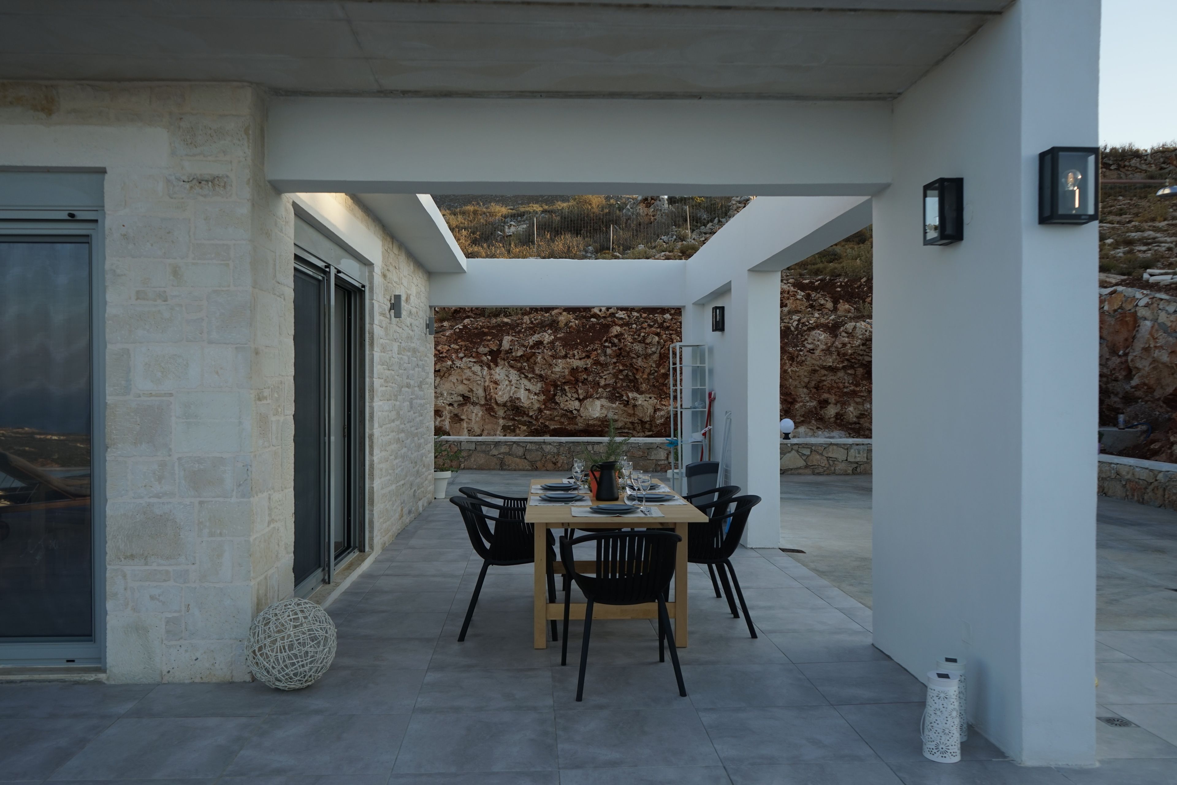 A modern outdoor dining area with a stone wall backdrop, a table with chairs, and a clear view of the surrounding landscape.