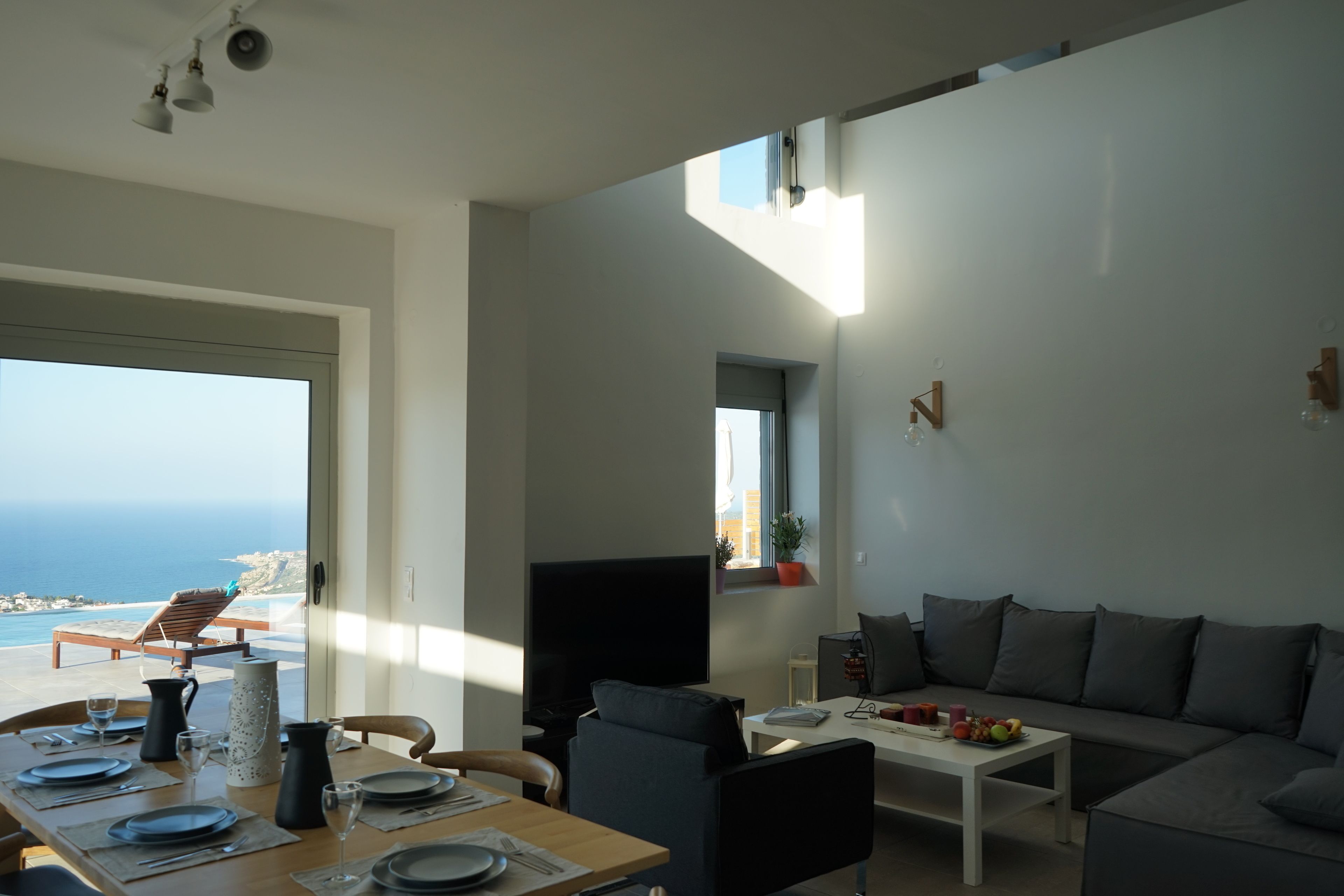 A modern living room with a dining area, a large flat-screen TV, and a view of the ocean.