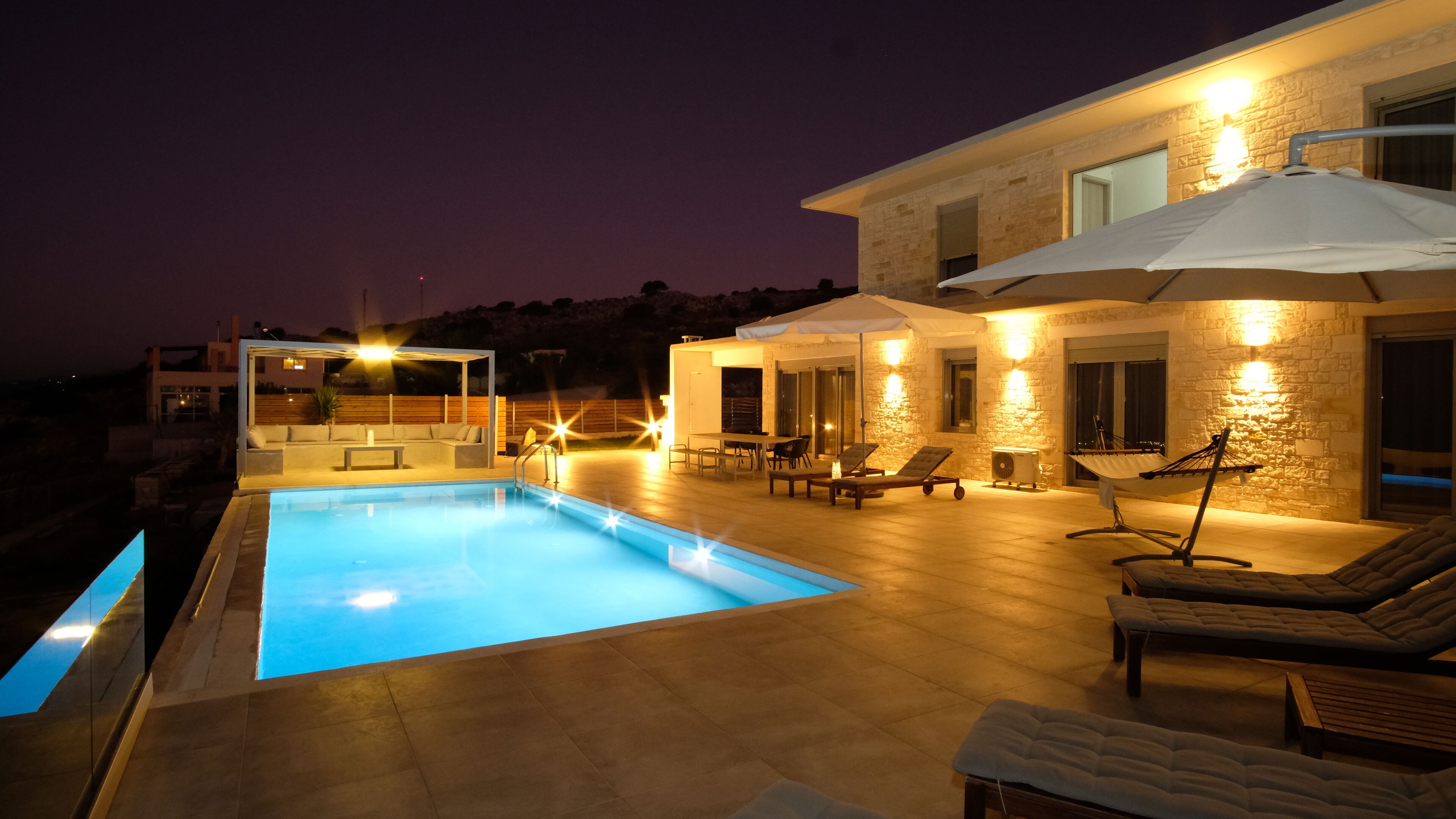 A modern poolside area with a rectangular pool, lounge chairs, and a covered seating area.
