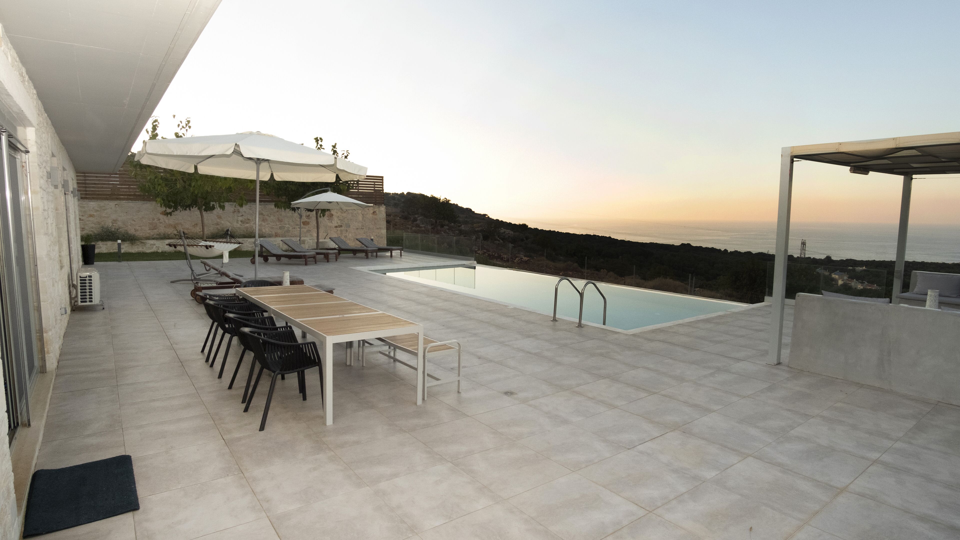 A rooftop terrace with a pool, lounge chairs, and umbrellas.