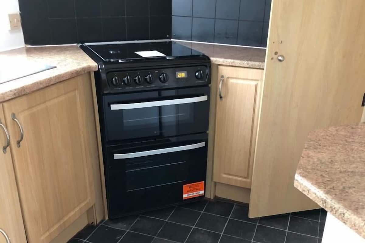 A compact kitchen with a black stove, wooden cabinets, and black tiled flooring.
