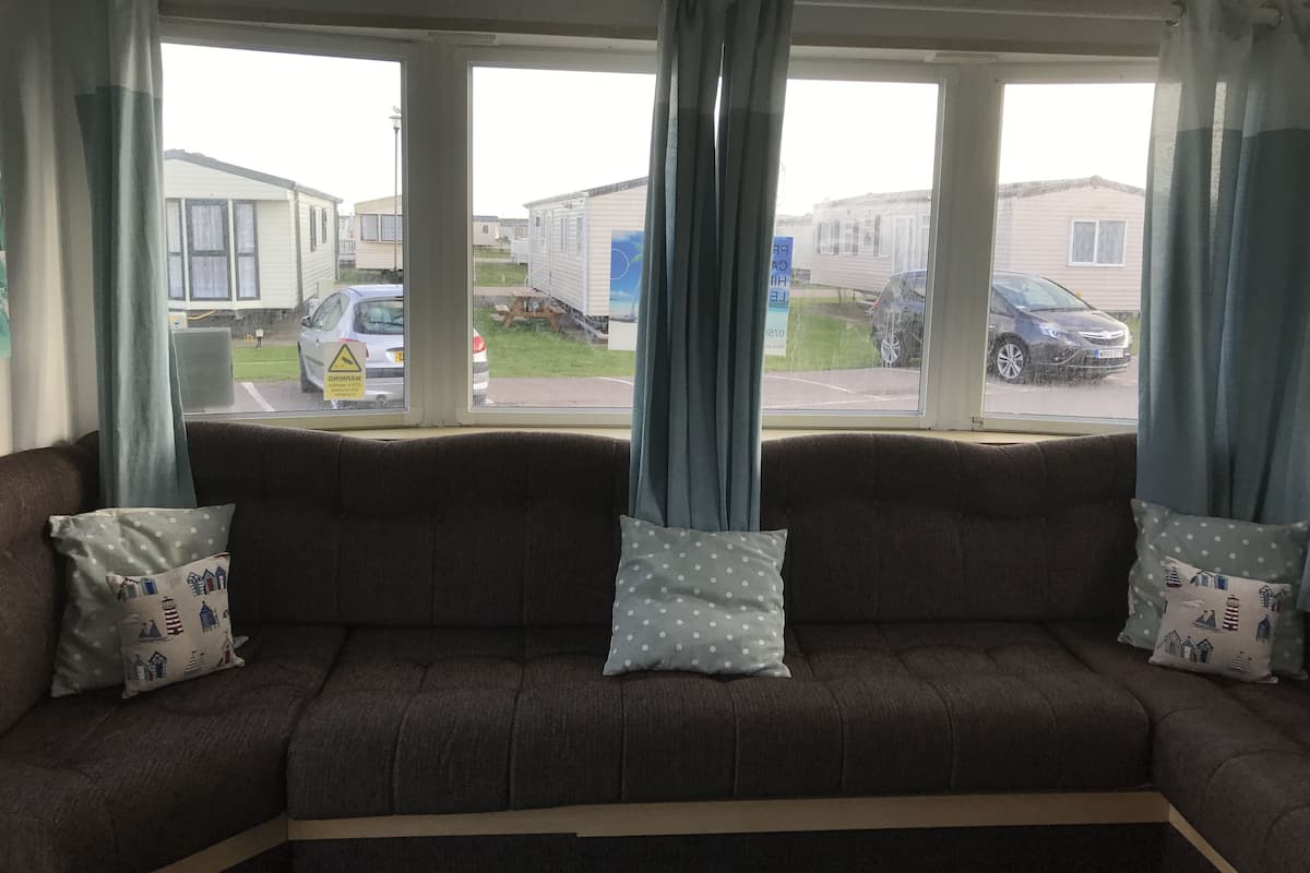A living room with a brown sofa, two patterned pillows, and a view of a street with parked cars and mobile homes.