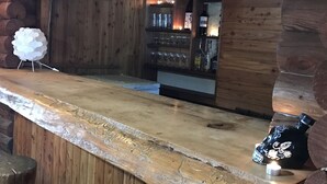 En rustik træbar med træbordplade, barstole og et køleskab fyldt med flasker.