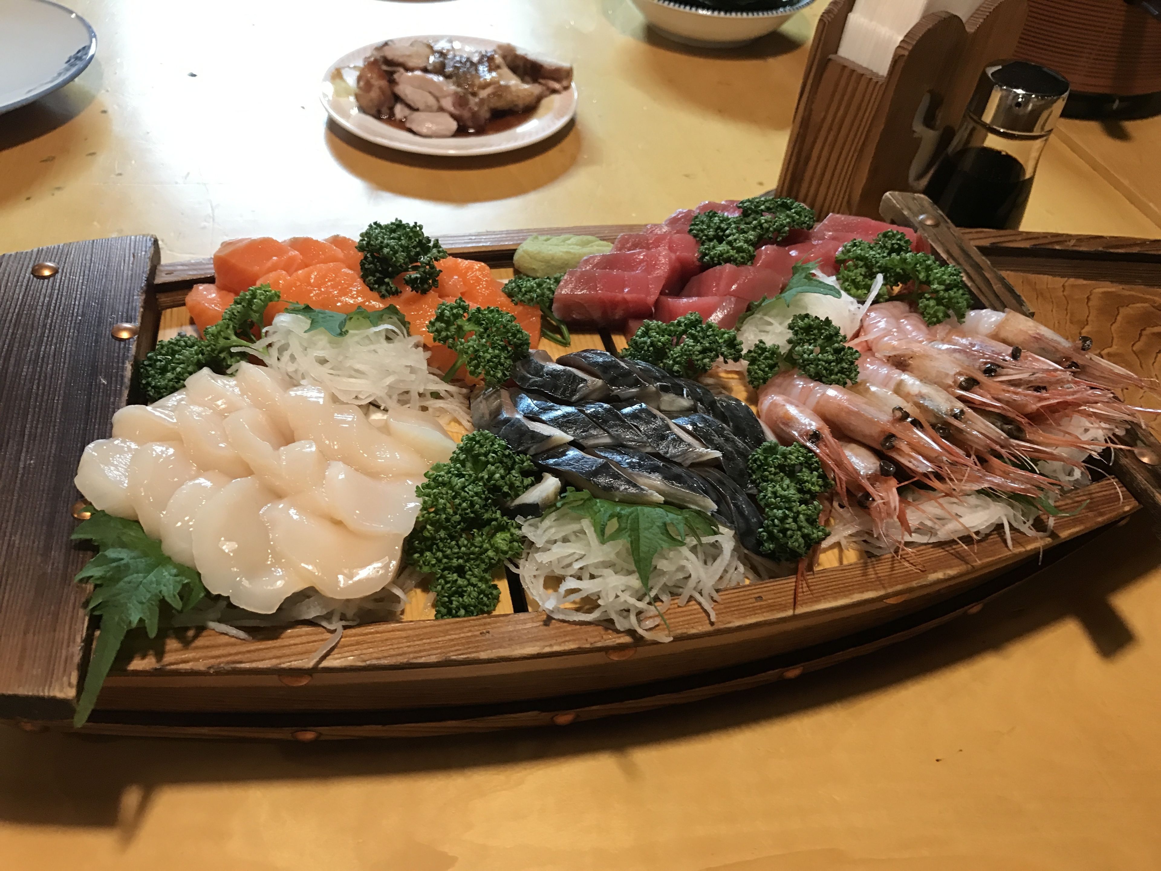 A wooden tray with various sashimi and seafood arranged on a table.