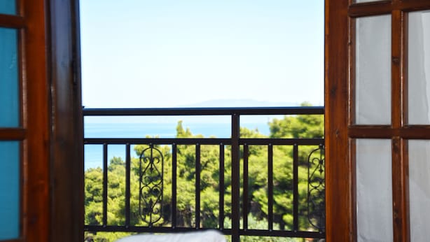 A balcony with a wooden railing and a view of a green landscape and a body of water.
