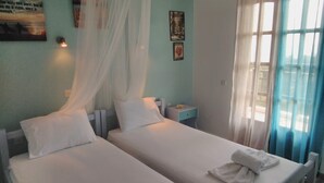 A room with two beds, a nightstand, a wall clock, and a window with curtains.