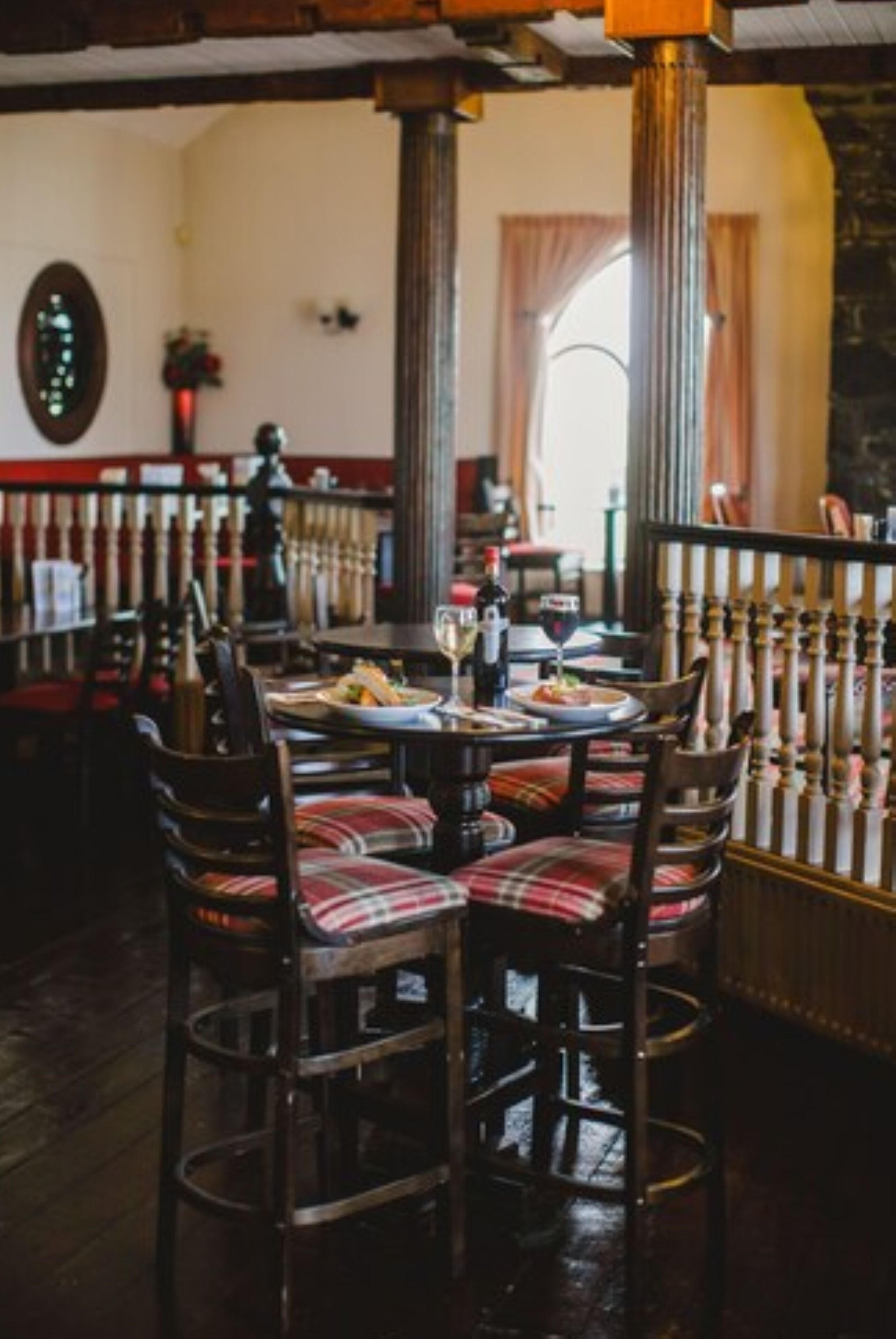 L’intérieur d’un restaurant, avec une table en bois dressée pour le repas, des chaises à motifs écossais et une colonne en arrière-plan.