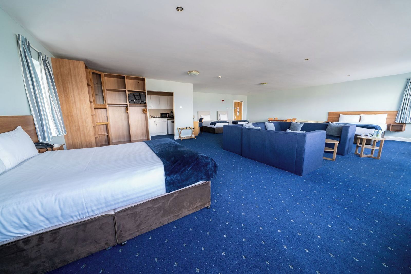 A hotel room with a large bed, a sofa, a desk, and a kitchenette.