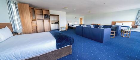 A hotel room with a large bed, a sofa, a desk, and a kitchenette.