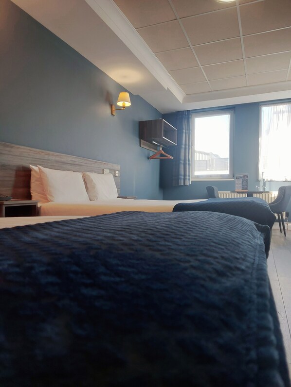 A hotel room with a large bed, a bedside table, a TV mounted on the wall, and a window with curtains.