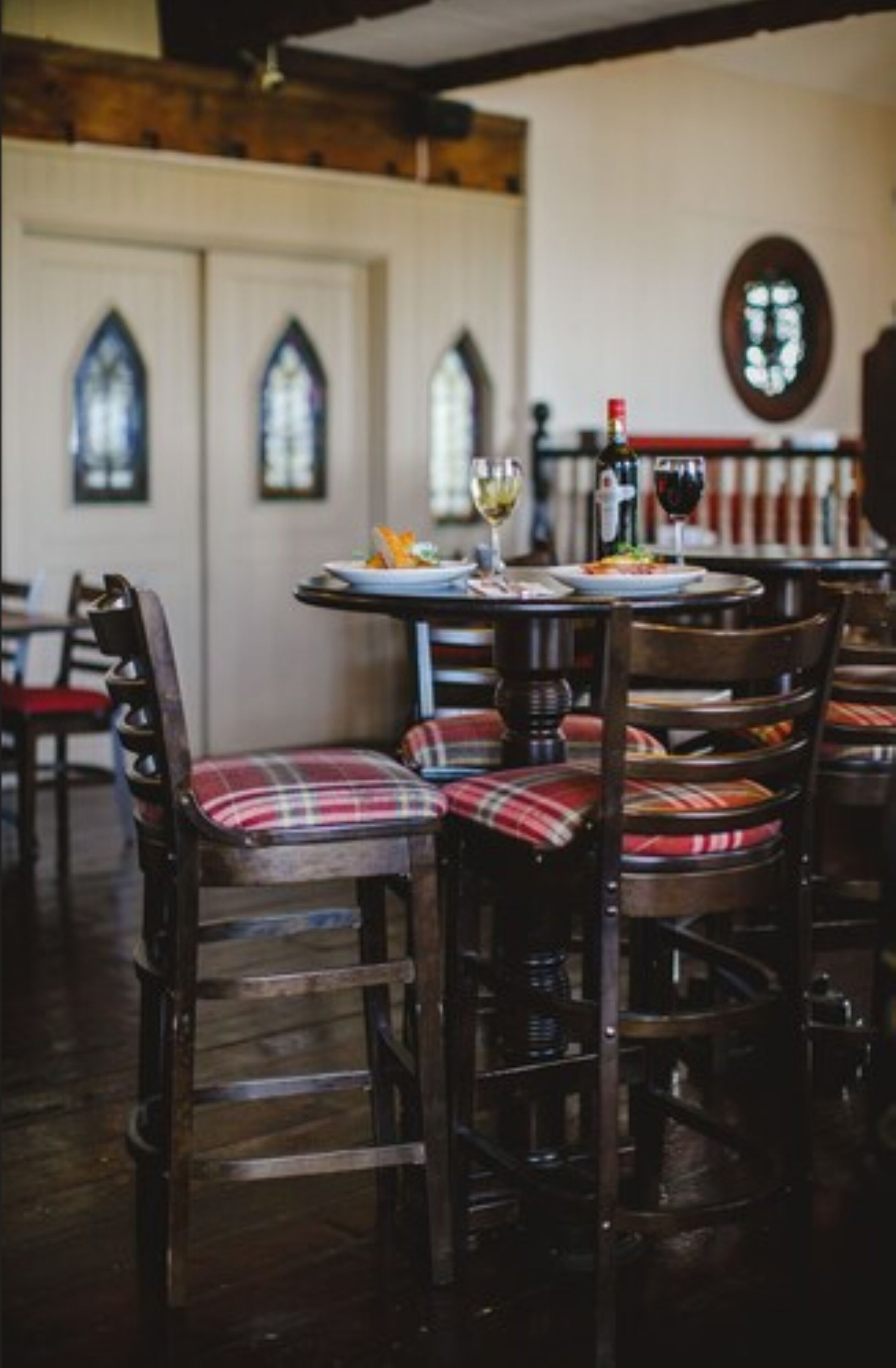 A dining area with wooden chairs and a table set for two, featuring plaid cushions.