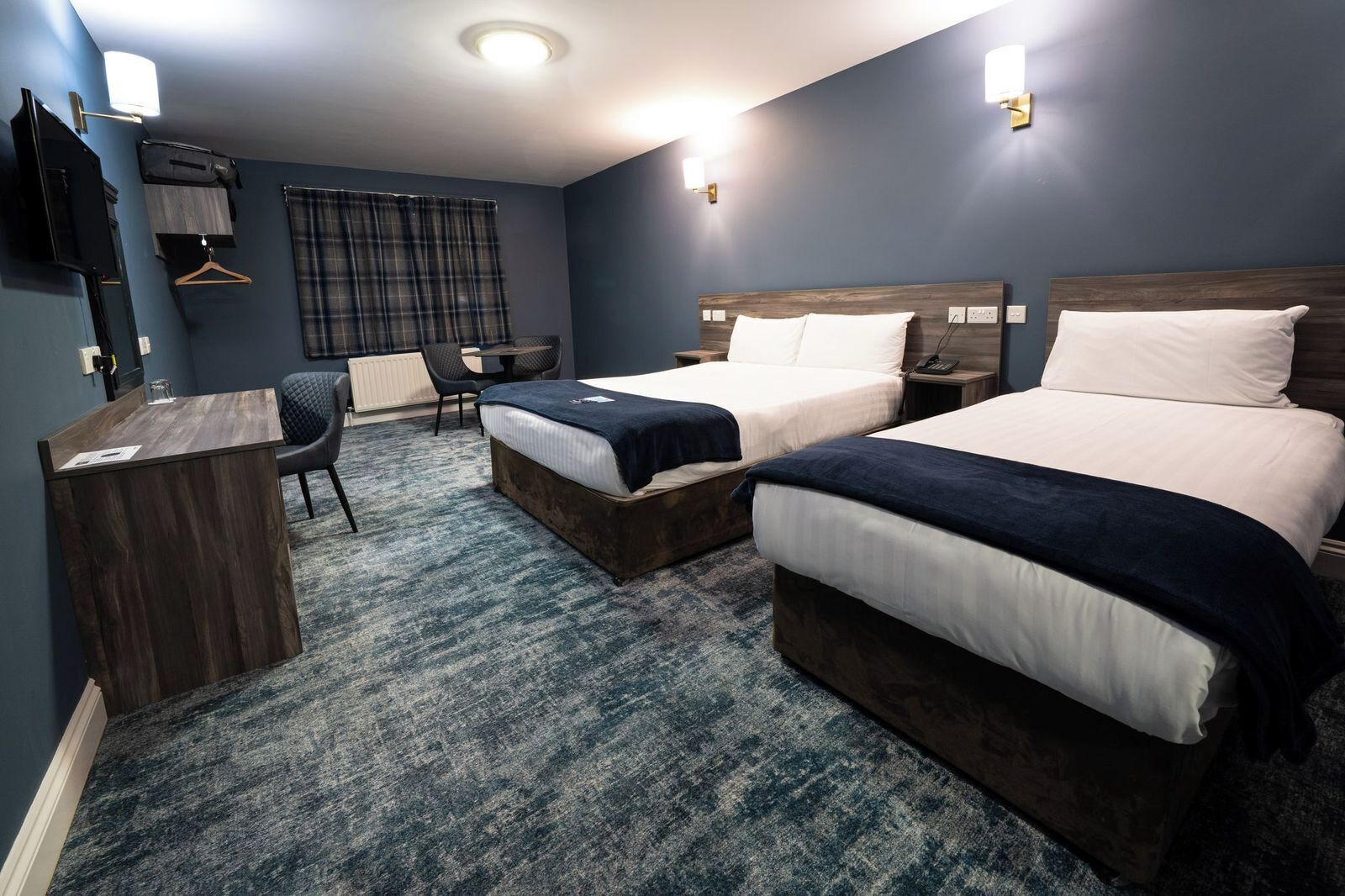 A hotel room with two beds, a desk, a chair, and a hanging coat rack.