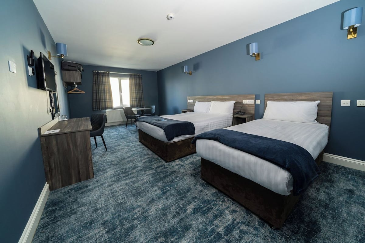 A hotel room with two beds, a desk, a chair, and a small table.