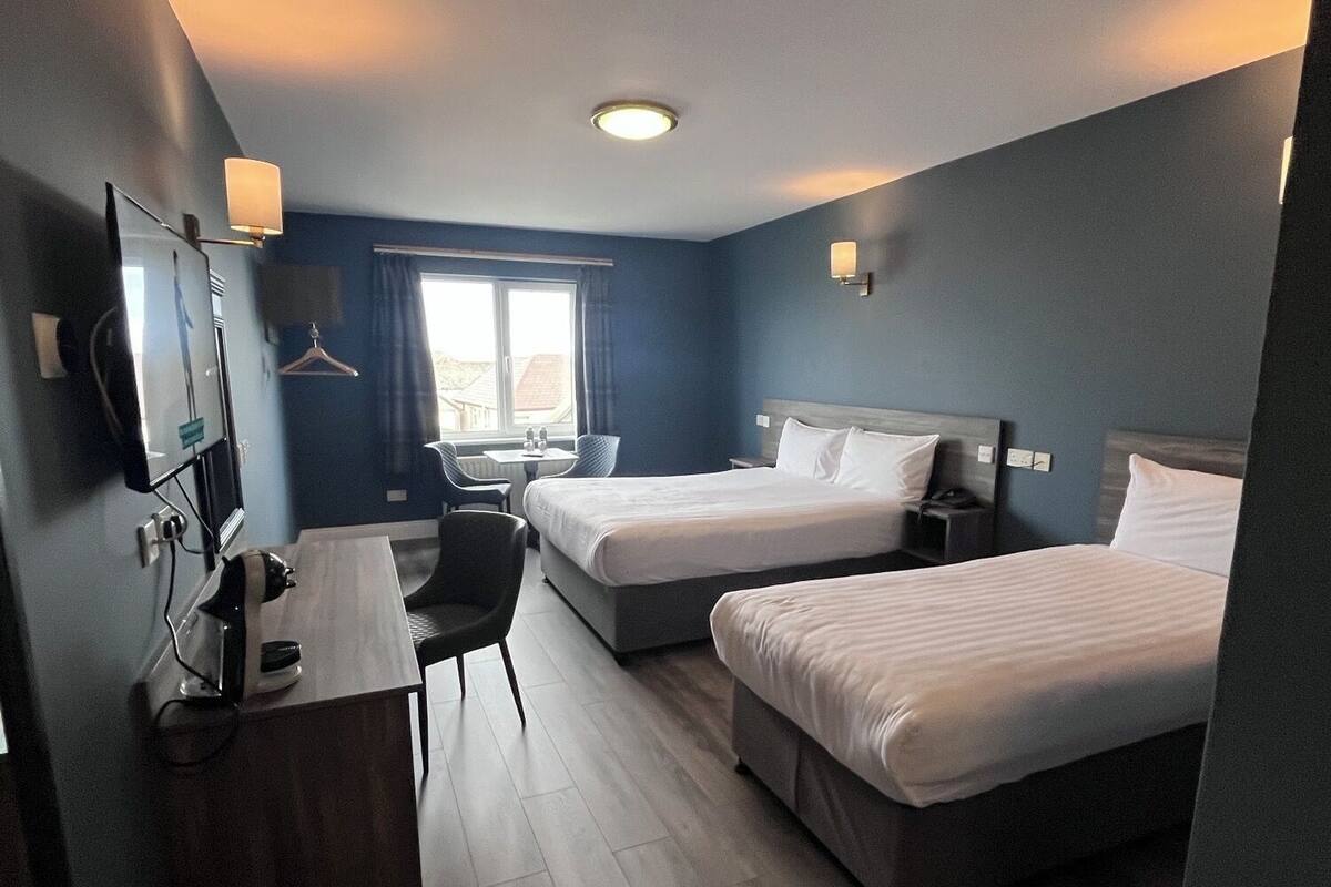 A hotel room with two beds, a desk, a chair, a TV, and a window with curtains.