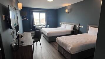 Une chambre d’hôtel avec deux lits, un bureau, une chaise, une télévision et une fenêtre avec des rideaux.
