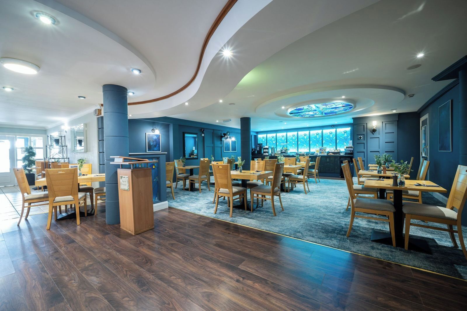 Un espace de restauration moderne avec des tables et des chaises en bois, une colonne centrale et une grande fenêtre offrant une vue dégagée.