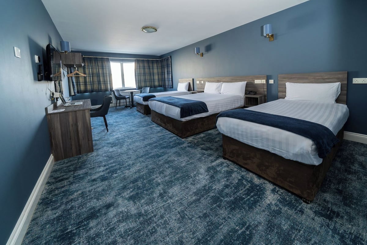 A hotel room with two beds, a desk, a chair, and a television.