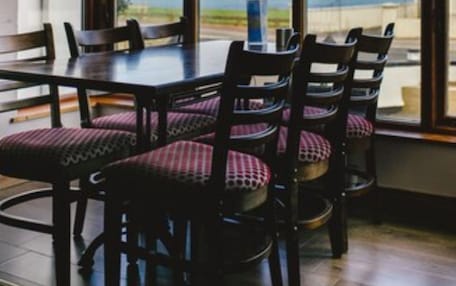 A dining area with a table and chairs, large windows, and a view of the outdoors.