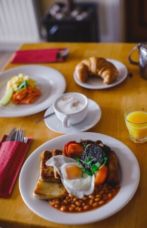 A breakfast setting with plates of food, a cup of coffee, and a glass of orange juice on a wooden table.