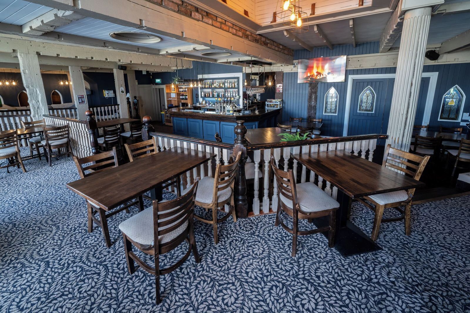 A restaurant with wooden tables and chairs, a bar area, and a patterned floor.